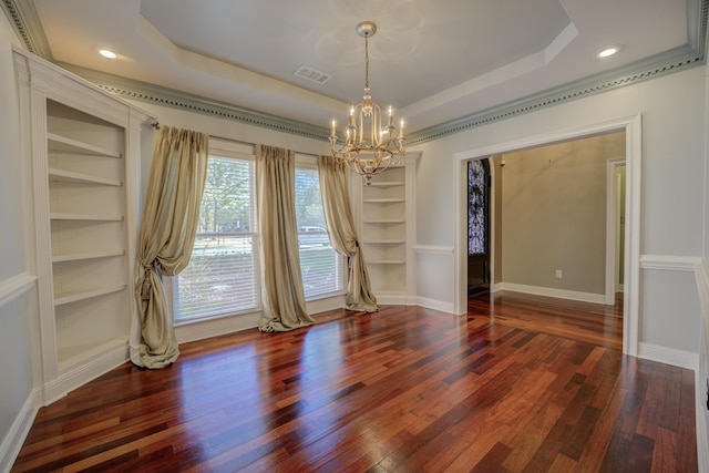 empty room with a notable chandelier, built in shelves, a raised ceiling, and dark wood-type flooring