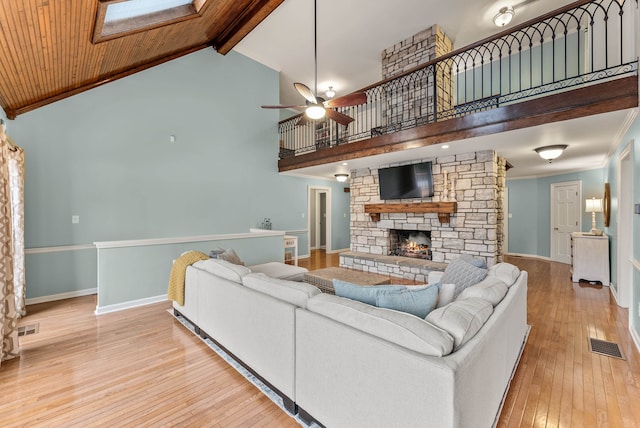 living room with ceiling fan, a skylight, high vaulted ceiling, and light hardwood / wood-style flooring