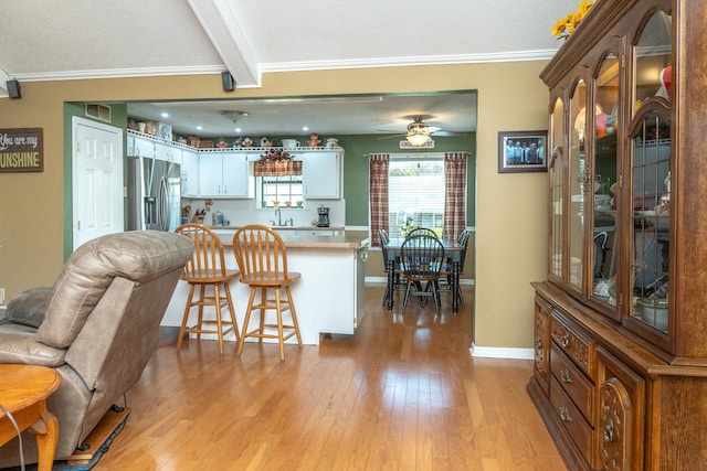 kitchen featuring white cabinets, kitchen peninsula, light hardwood / wood-style flooring, a kitchen bar, and stainless steel fridge with ice dispenser