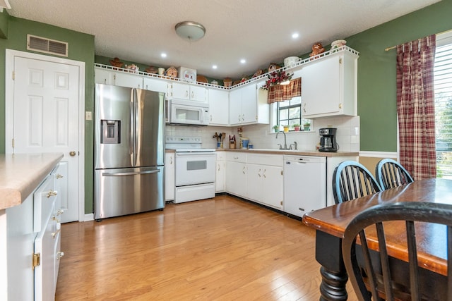 kitchen featuring white cabinetry, sink, backsplash, white appliances, and light wood-type flooring