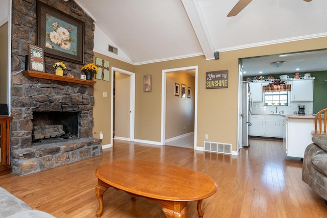 living room featuring crown molding, vaulted ceiling with beams, ceiling fan, a fireplace, and light hardwood / wood-style floors