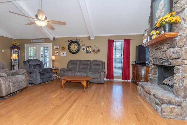 living room featuring ceiling fan, vaulted ceiling with beams, a stone fireplace, light hardwood / wood-style floors, and ornamental molding