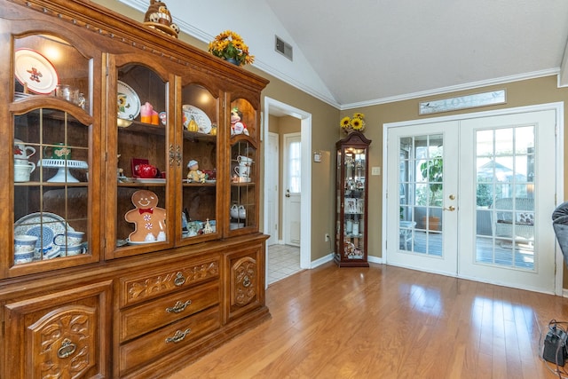 doorway with french doors, ornamental molding, lofted ceiling, and light wood-type flooring