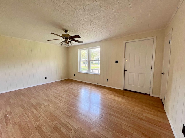 spare room with ceiling fan, wood walls, and light hardwood / wood-style flooring