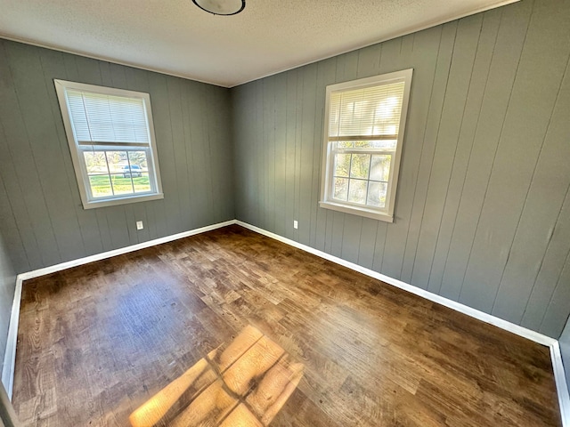 empty room with wood walls, plenty of natural light, a textured ceiling, and hardwood / wood-style flooring