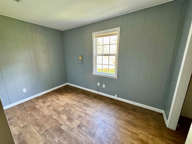 unfurnished room featuring wood walls, hardwood / wood-style floors, and a textured ceiling