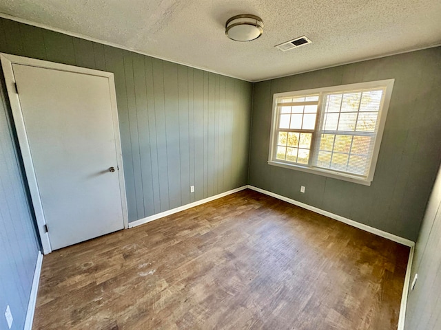 empty room featuring hardwood / wood-style floors, wood walls, and a textured ceiling