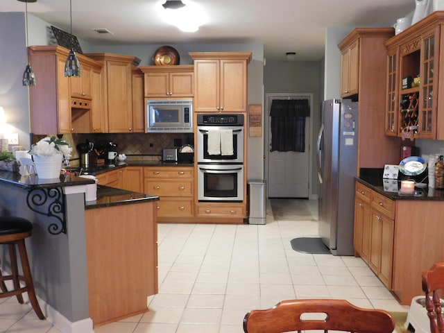 kitchen featuring light tile patterned flooring, appliances with stainless steel finishes, a kitchen bar, decorative backsplash, and hanging light fixtures