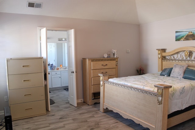 bedroom featuring ensuite bath, vaulted ceiling, and light hardwood / wood-style flooring