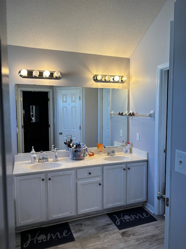 bathroom with vaulted ceiling, vanity, a textured ceiling, and hardwood / wood-style flooring