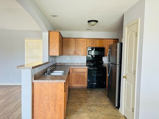 kitchen with sink, kitchen peninsula, a textured ceiling, black appliances, and hardwood / wood-style flooring