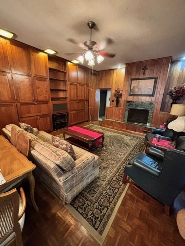 living room with ceiling fan, a premium fireplace, dark parquet floors, a textured ceiling, and wooden walls