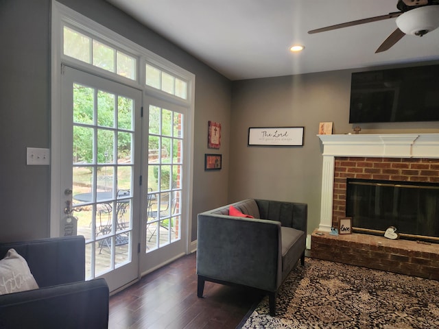 living room with a fireplace, ceiling fan, and dark wood-type flooring