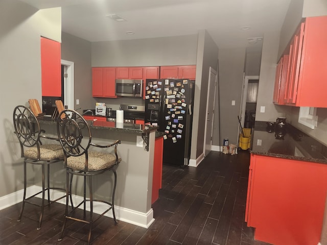 kitchen featuring dark hardwood / wood-style flooring, kitchen peninsula, a breakfast bar area, and appliances with stainless steel finishes