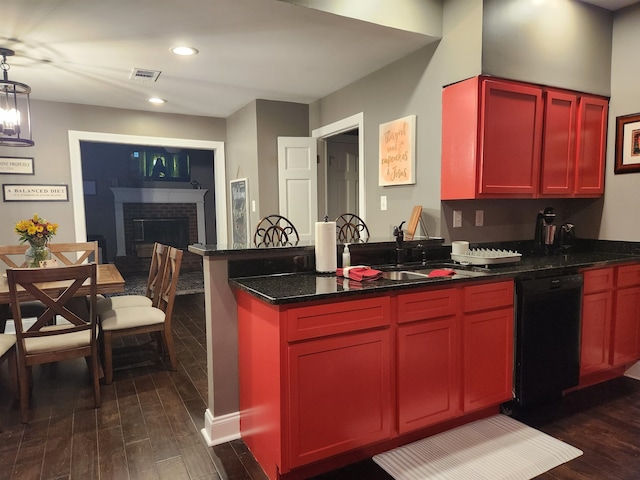 kitchen featuring dark hardwood / wood-style flooring, a brick fireplace, dark stone countertops, black dishwasher, and hanging light fixtures