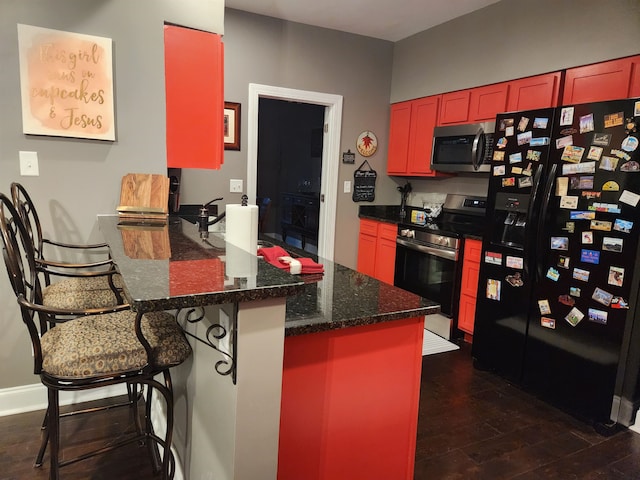 kitchen featuring dark stone counters, a kitchen breakfast bar, dark hardwood / wood-style floors, kitchen peninsula, and stainless steel appliances