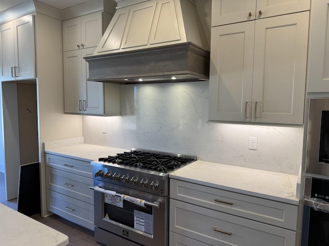 kitchen featuring tasteful backsplash, premium range hood, high end range, and light stone countertops