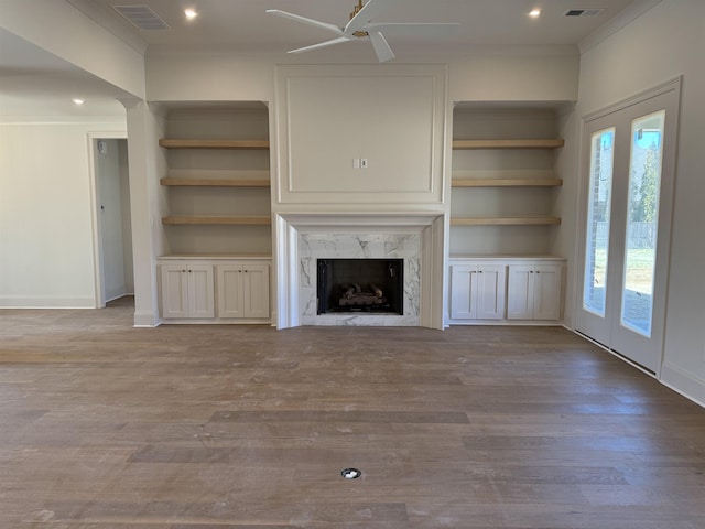 unfurnished living room featuring crown molding, visible vents, a ceiling fan, a high end fireplace, and wood finished floors