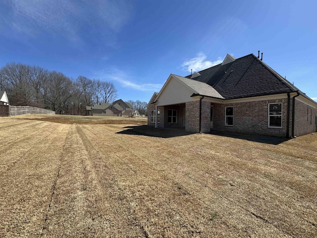 view of side of property featuring a shingled roof, fence, a lawn, and brick siding