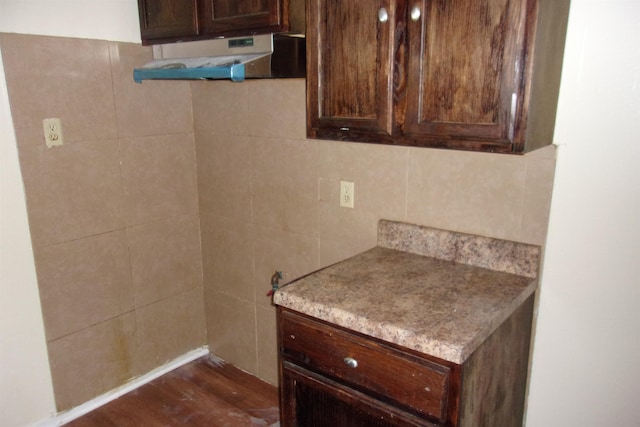 kitchen with dark brown cabinetry, dark wood-type flooring, and tile walls