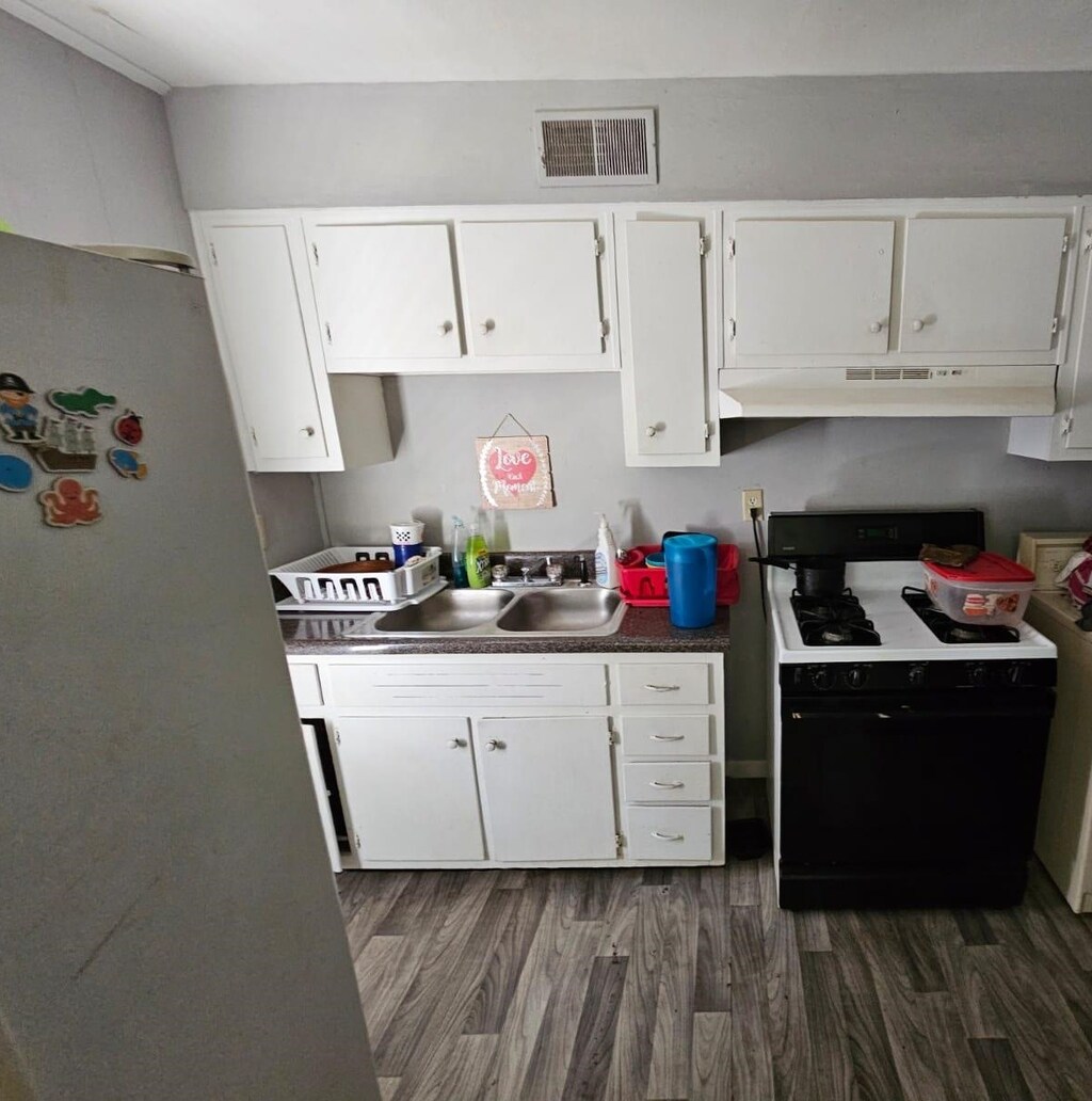 3263 Sunrise Ave, Memphis, TN 38127 - kitchen with black range with gas stovetop, under cabinet range hood, freestanding refrigerator, a sink, and dark wood-style flooring
