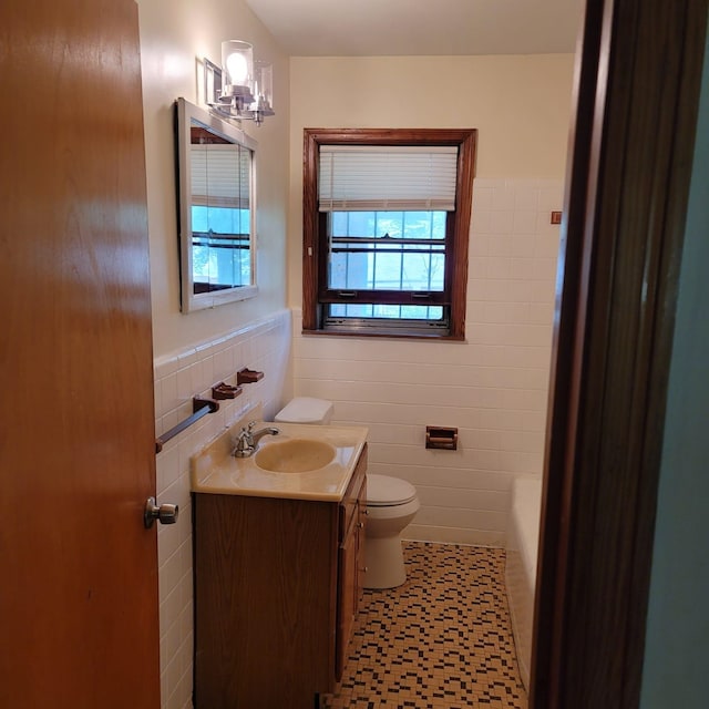 bathroom with a wealth of natural light, vanity, tile walls, and toilet