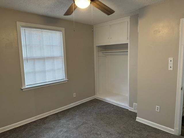 unfurnished bedroom with ceiling fan, a closet, a textured ceiling, and dark colored carpet