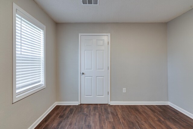 empty room featuring a textured ceiling, a wealth of natural light, and dark wood-type flooring