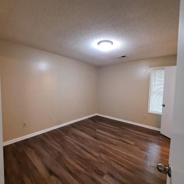 empty room with a textured ceiling and dark hardwood / wood-style flooring