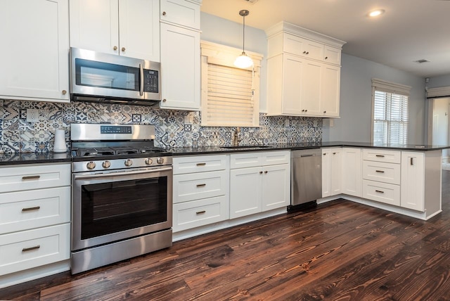 kitchen featuring kitchen peninsula, stainless steel appliances, dark wood-type flooring, sink, and pendant lighting