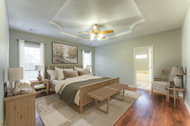 bedroom featuring connected bathroom, ceiling fan, a raised ceiling, a textured ceiling, and hardwood / wood-style flooring