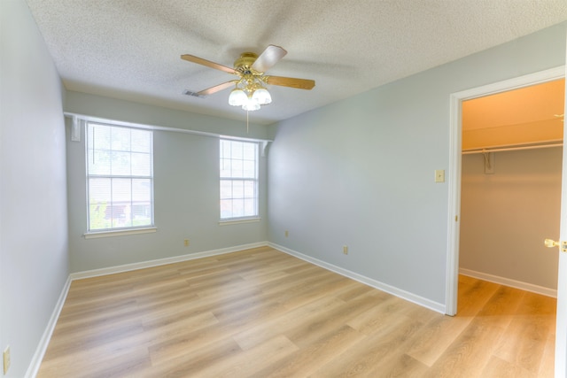 unfurnished bedroom featuring ceiling fan, a spacious closet, light wood-type flooring, a textured ceiling, and a closet