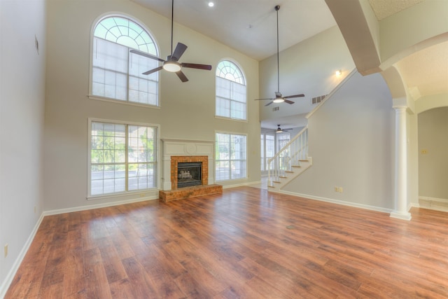 unfurnished living room with a brick fireplace, light hardwood / wood-style flooring, high vaulted ceiling, and a healthy amount of sunlight