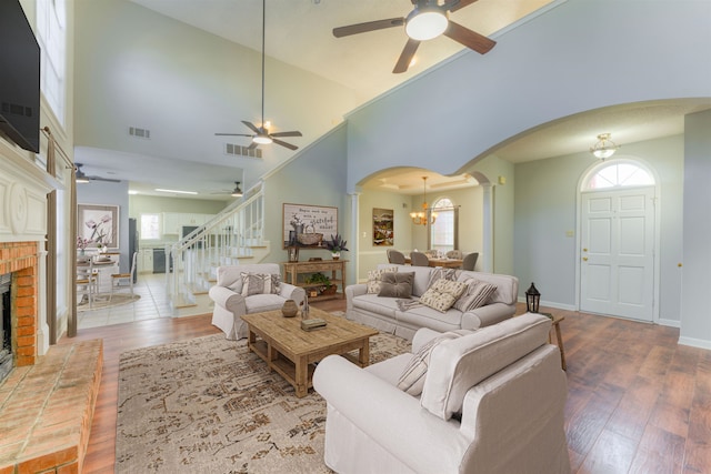 living room with a fireplace, hardwood / wood-style floors, high vaulted ceiling, and ceiling fan with notable chandelier