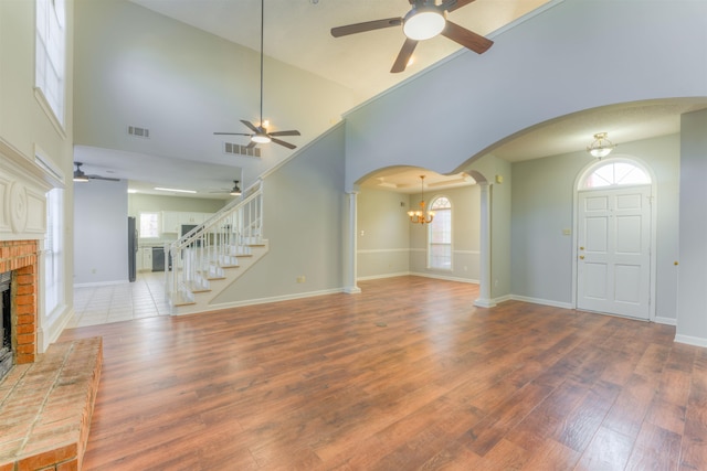 unfurnished living room featuring hardwood / wood-style flooring, ceiling fan with notable chandelier, high vaulted ceiling, and a brick fireplace