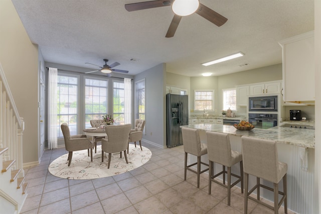 kitchen with black appliances, a kitchen breakfast bar, white cabinets, a textured ceiling, and light stone counters