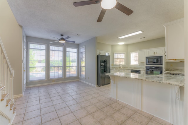 kitchen with black appliances, kitchen peninsula, light tile patterned floors, light stone counters, and white cabinetry