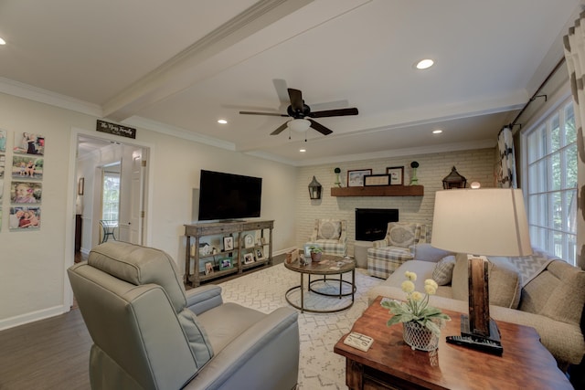 living room with ceiling fan, beamed ceiling, wood-type flooring, a fireplace, and ornamental molding