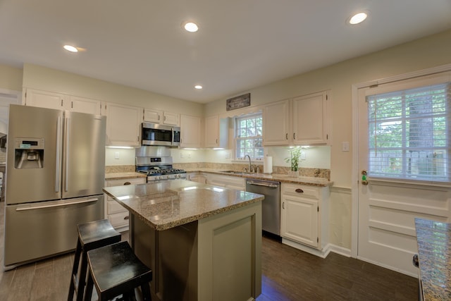 kitchen featuring light stone countertops, appliances with stainless steel finishes, a center island, dark hardwood / wood-style floors, and white cabinetry