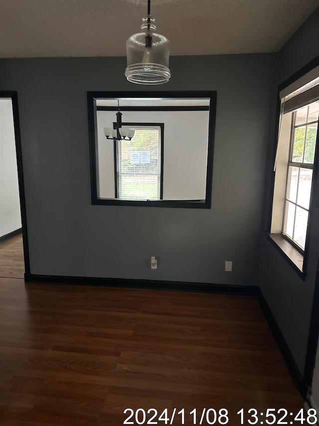 spare room with dark wood-type flooring and an inviting chandelier