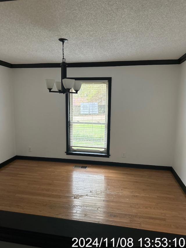 unfurnished dining area with hardwood / wood-style floors, ornamental molding, a textured ceiling, and a notable chandelier