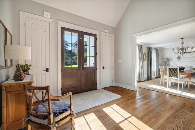 entrance foyer featuring vaulted ceiling, light wood-type flooring, french doors, and an inviting chandelier