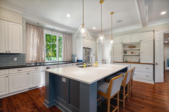 kitchen featuring pendant lighting, a kitchen island with sink, sink, dark stone countertops, and dark hardwood / wood-style flooring