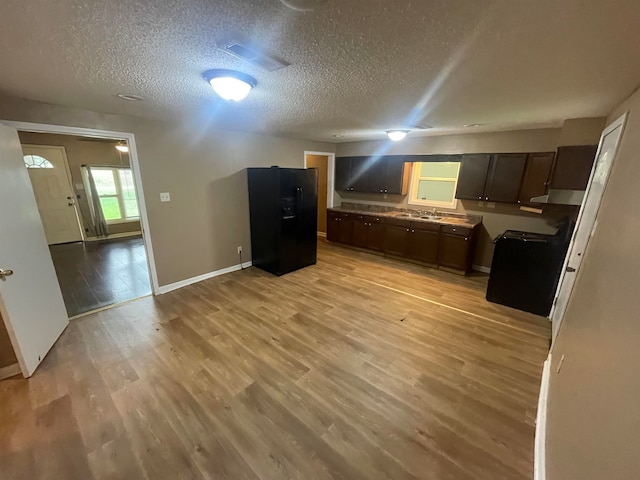 kitchen featuring stove, black fridge with ice dispenser, dark brown cabinets, a textured ceiling, and light hardwood / wood-style flooring