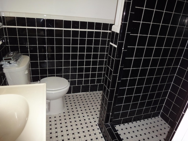 bathroom with toilet, a tile shower, and tile walls