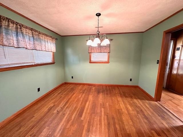 empty room featuring ornamental molding, light wood-type flooring, a textured ceiling, and a notable chandelier