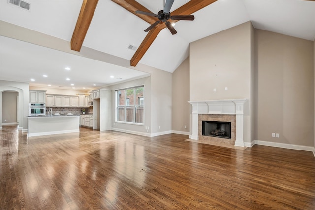 unfurnished living room with ceiling fan, sink, wood-type flooring, vaulted ceiling with beams, and a tiled fireplace