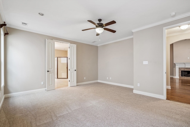 spare room featuring ceiling fan, ornamental molding, light carpet, and a tile fireplace