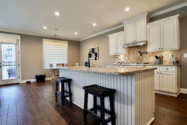 kitchen featuring a kitchen bar, light stone counters, dark hardwood / wood-style flooring, an island with sink, and white cabinets