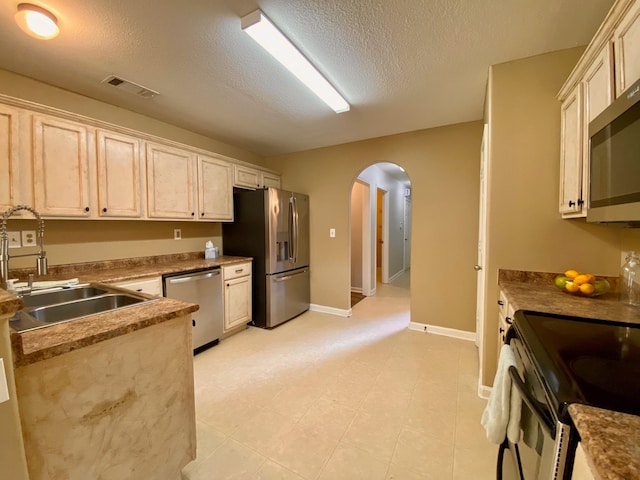 kitchen with a textured ceiling, sink, stainless steel appliances, and cream cabinetry